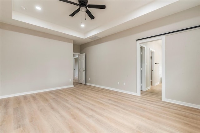 spare room featuring a tray ceiling, ceiling fan, and light wood-type flooring