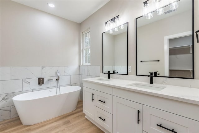 bathroom with hardwood / wood-style floors, vanity, a bath, and tile walls