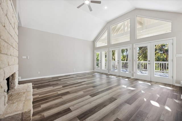 unfurnished living room featuring french doors, vaulted ceiling, ceiling fan, hardwood / wood-style floors, and a stone fireplace