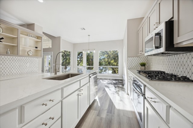 kitchen with light stone counters, stainless steel appliances, sink, white cabinetry, and hanging light fixtures