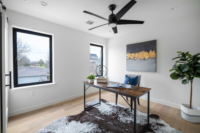 office space featuring a barn door, ceiling fan, and light hardwood / wood-style flooring