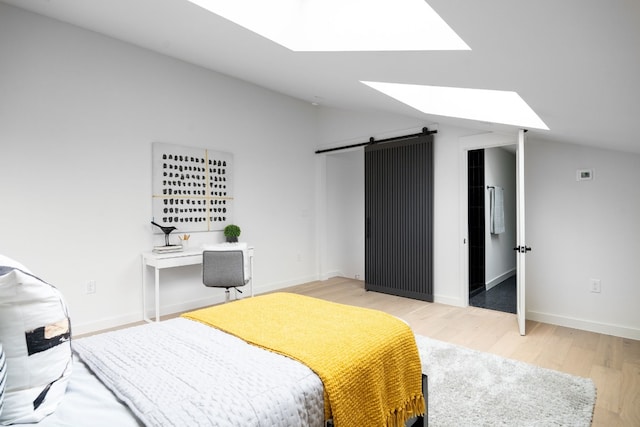 bedroom featuring vaulted ceiling with skylight, a barn door, and light hardwood / wood-style flooring