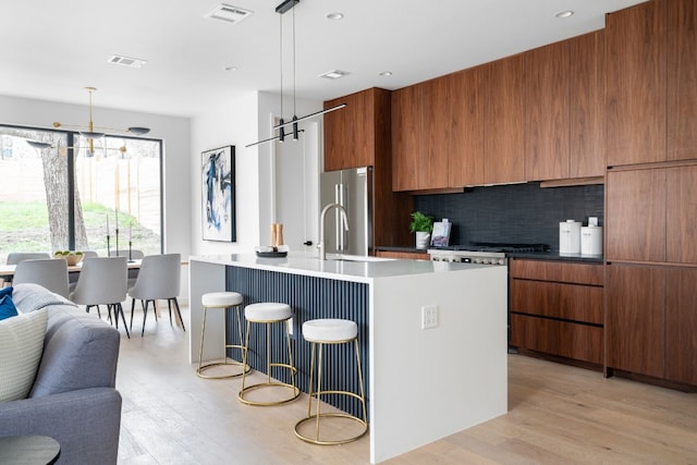 kitchen with hanging light fixtures, light wood-type flooring, an island with sink, tasteful backsplash, and high end fridge