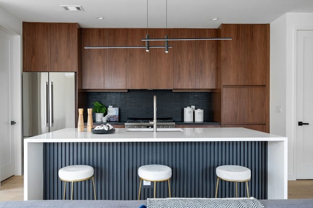 kitchen with backsplash, a kitchen island with sink, pendant lighting, and light hardwood / wood-style floors