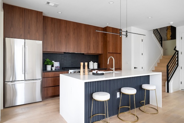 kitchen featuring pendant lighting, a center island with sink, stainless steel fridge, tasteful backsplash, and light hardwood / wood-style floors