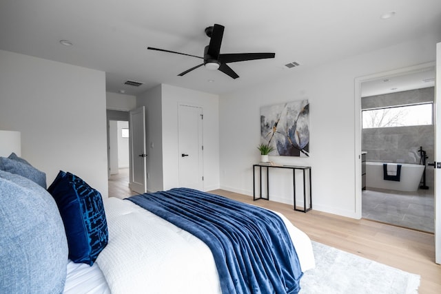 bedroom with ensuite bathroom, light hardwood / wood-style floors, tile walls, and ceiling fan