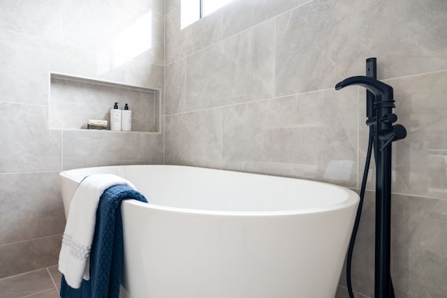 bathroom featuring tile patterned flooring, a tub to relax in, and tile walls