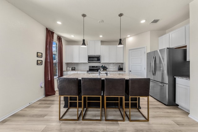 kitchen featuring backsplash, a kitchen island with sink, light stone countertops, appliances with stainless steel finishes, and white cabinetry