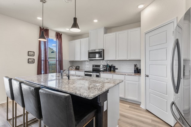 kitchen featuring white cabinetry, stainless steel appliances, pendant lighting, a center island with sink, and light wood-type flooring