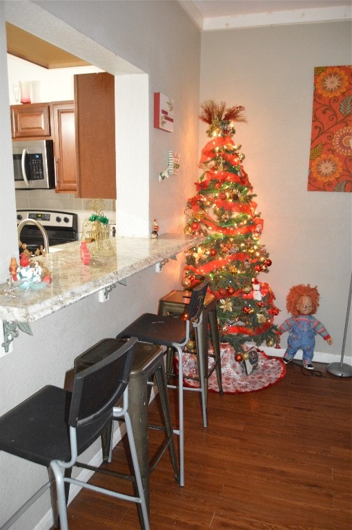 kitchen with light stone countertops, a breakfast bar, dark wood-type flooring, and appliances with stainless steel finishes