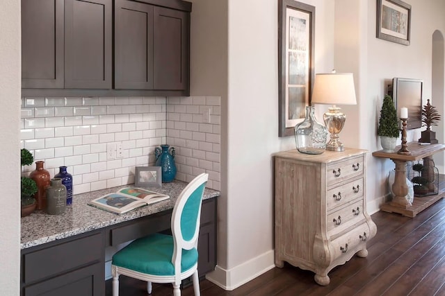 interior space featuring dark wood-type flooring, tasteful backsplash, light stone counters, gray cabinets, and built in desk