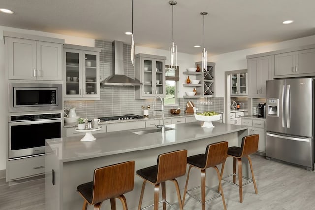 kitchen with a kitchen bar, wall chimney exhaust hood, stainless steel appliances, sink, and an island with sink