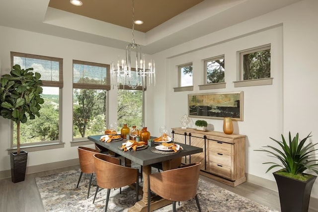 dining room featuring an inviting chandelier, a raised ceiling, and light hardwood / wood-style flooring