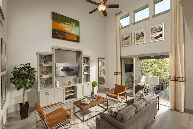 living room with ceiling fan, a healthy amount of sunlight, a high ceiling, and light wood-type flooring