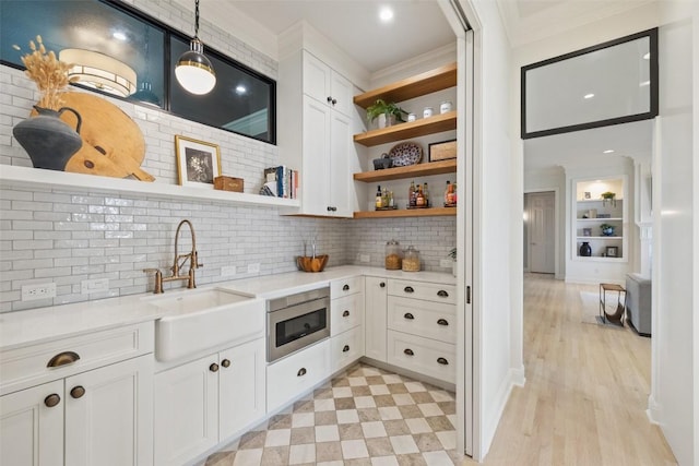 interior space featuring stainless steel microwave, sink, hanging light fixtures, crown molding, and white cabinets