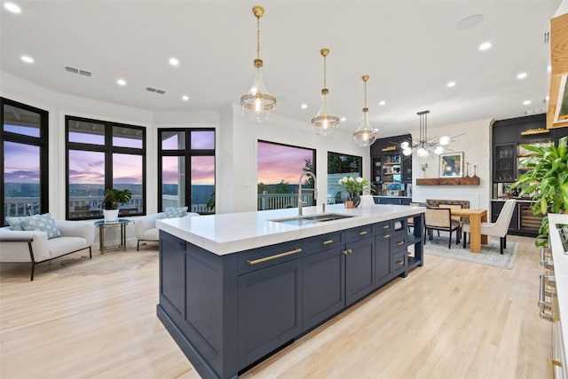 kitchen featuring open floor plan, light countertops, a center island with sink, and decorative light fixtures