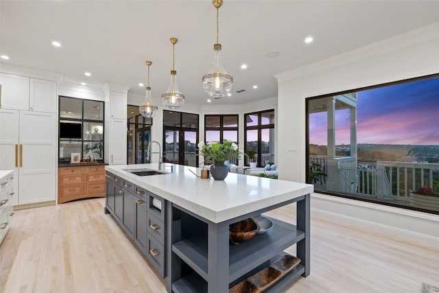 kitchen with a sink, white cabinetry, open shelves, a center island with sink, and pendant lighting