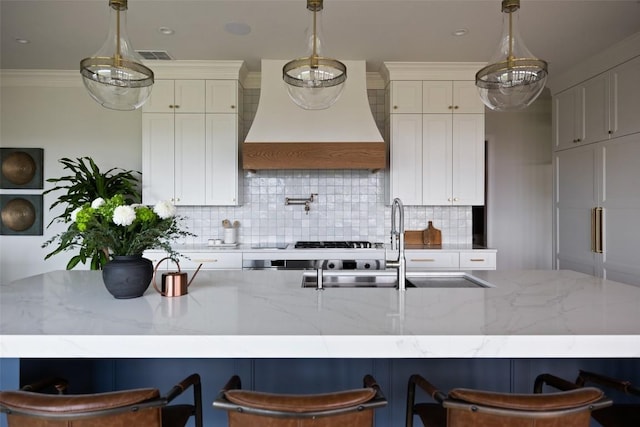 kitchen with a kitchen bar, custom range hood, light stone counters, and pendant lighting