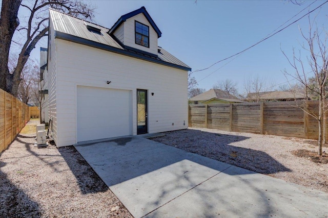 rear view of property featuring cooling unit, fence, metal roof, and concrete driveway