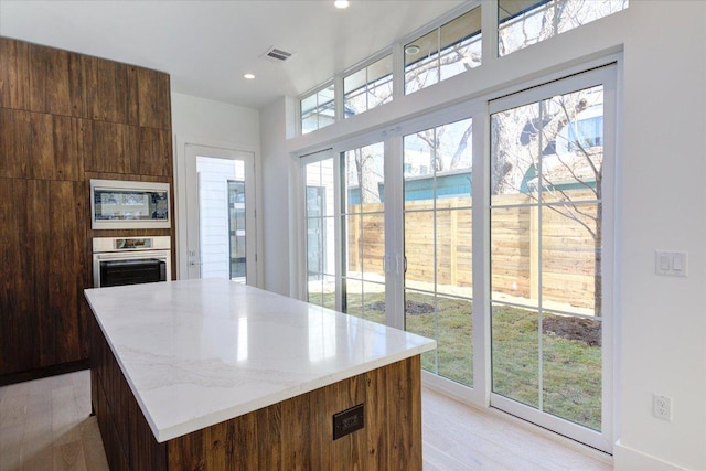 kitchen with a center island, recessed lighting, light wood-style flooring, built in microwave, and oven