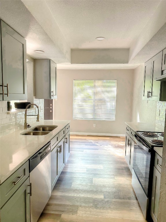 kitchen with sink, tasteful backsplash, light hardwood / wood-style floors, a textured ceiling, and appliances with stainless steel finishes