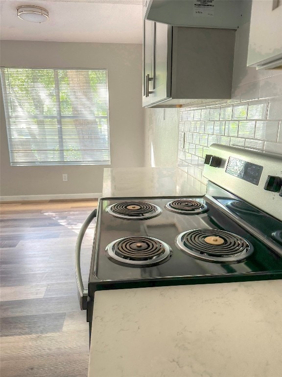 kitchen with light wood-type flooring, backsplash, gray cabinetry, stainless steel electric stove, and exhaust hood