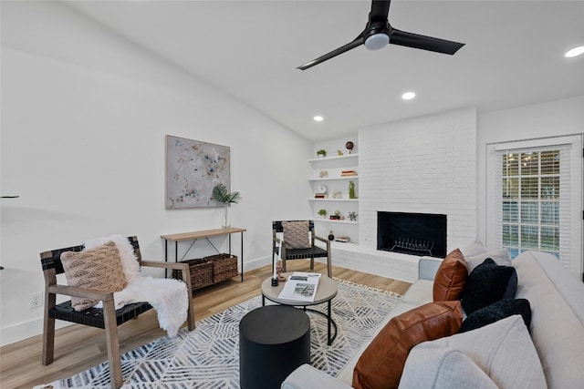 living room with a brick fireplace, ceiling fan, vaulted ceiling, and light wood-type flooring