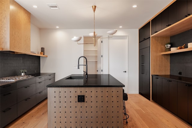 kitchen with tasteful backsplash, sink, a center island with sink, light hardwood / wood-style flooring, and stainless steel gas stovetop