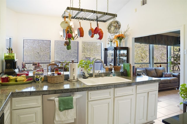 kitchen featuring stainless steel dishwasher, sink, light tile patterned floors, an inviting chandelier, and lofted ceiling