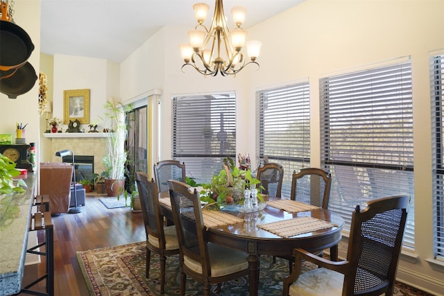 dining area featuring dark wood-type flooring, a tile fireplace, and an inviting chandelier