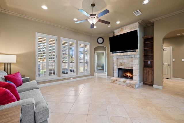 tiled living room featuring a stone fireplace, ceiling fan, built in shelves, and ornamental molding