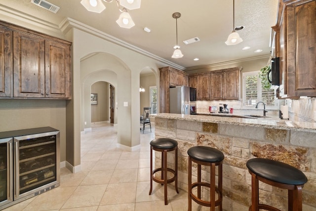 kitchen featuring wine cooler, stainless steel fridge, light tile patterned floors, ornamental molding, and light stone counters