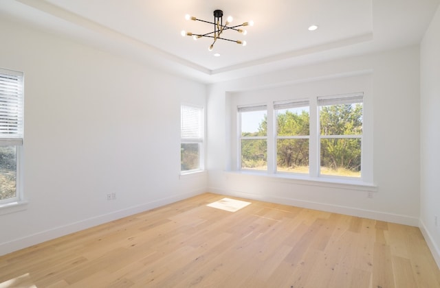 spare room featuring a tray ceiling, an inviting chandelier, a healthy amount of sunlight, and light hardwood / wood-style floors