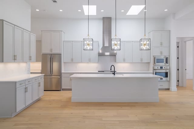 kitchen with a skylight, wall chimney exhaust hood, stainless steel appliances, light hardwood / wood-style flooring, and decorative light fixtures