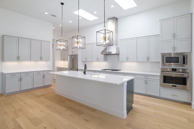 kitchen featuring a skylight, hanging light fixtures, light hardwood / wood-style floors, a kitchen island with sink, and appliances with stainless steel finishes