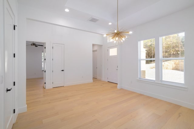 unfurnished room with ceiling fan with notable chandelier and light hardwood / wood-style flooring