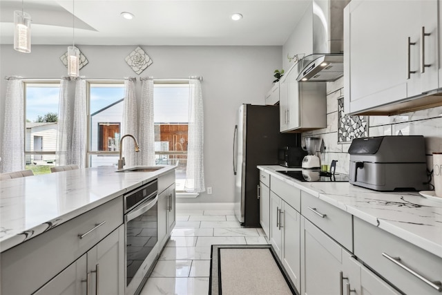 kitchen with sink, wall chimney exhaust hood, decorative backsplash, appliances with stainless steel finishes, and decorative light fixtures