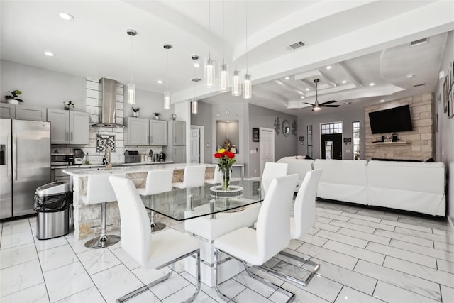 dining space with ceiling fan, beam ceiling, and a fireplace