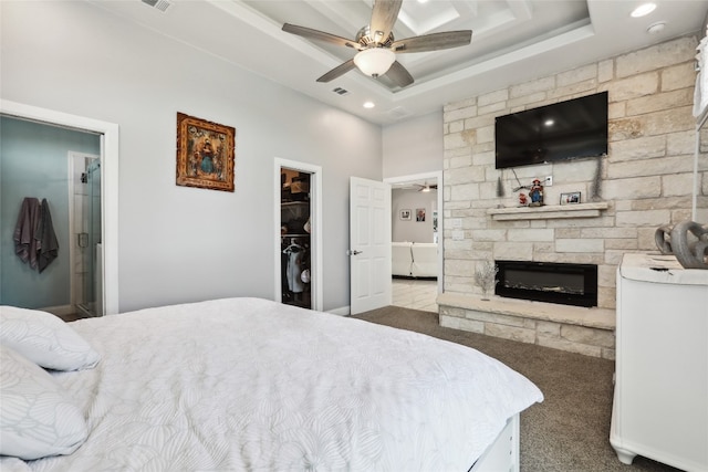 carpeted bedroom with a spacious closet, ceiling fan, a raised ceiling, a fireplace, and a closet