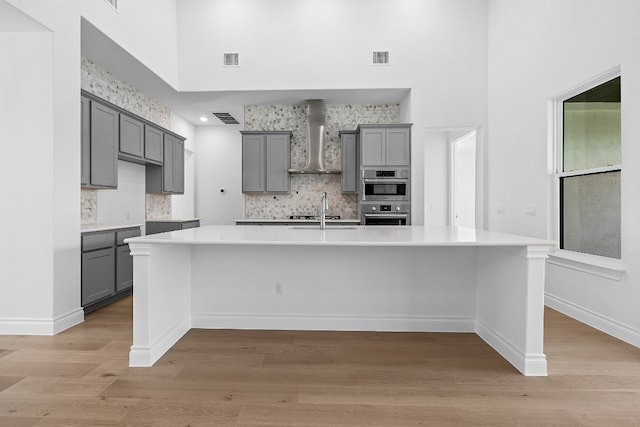 kitchen with a towering ceiling, a spacious island, wall chimney exhaust hood, and gray cabinetry