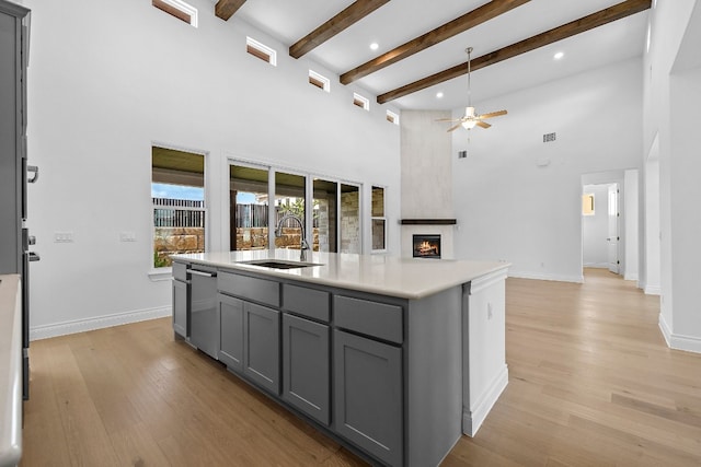 kitchen featuring stainless steel dishwasher, sink, light hardwood / wood-style flooring, gray cabinets, and an island with sink