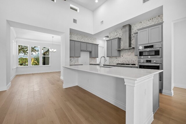 kitchen featuring a towering ceiling, light hardwood / wood-style floors, wall chimney exhaust hood, and an island with sink