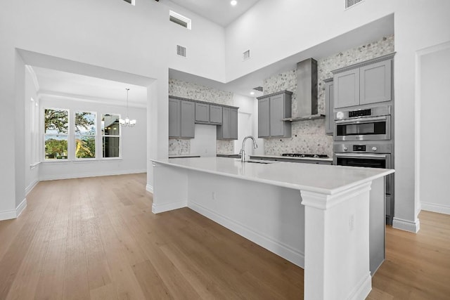 409 Mayapple, Horseshoe Bay, TX 78657 - kitchen featuring wall chimney range hood, gray cabinets, a sink, a chandelier, and light wood-style floors