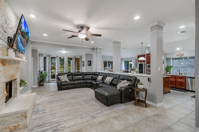 tiled living room with ornate columns, ornamental molding, ceiling fan, sink, and a fireplace