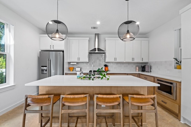 kitchen with a kitchen island with sink, white cabinetry, wall chimney exhaust hood, and stainless steel appliances