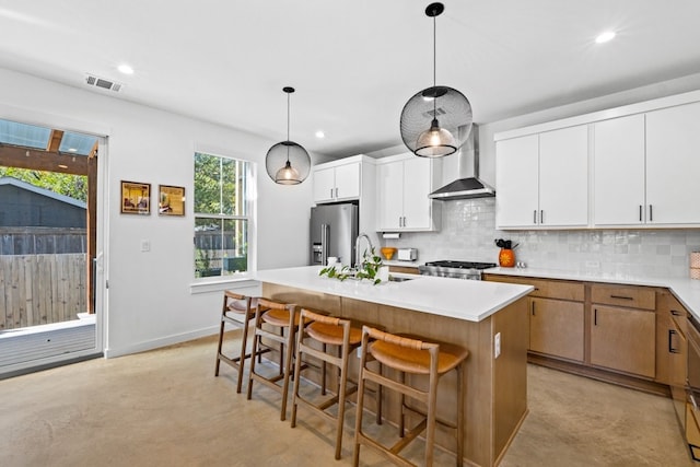 kitchen with backsplash, a center island with sink, hanging light fixtures, wall chimney exhaust hood, and white cabinetry