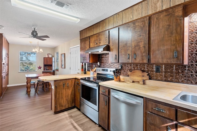 kitchen featuring ceiling fan with notable chandelier, a textured ceiling, tasteful backsplash, light hardwood / wood-style floors, and stainless steel appliances