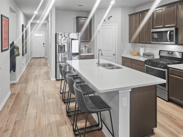 kitchen featuring stainless steel appliances, light hardwood / wood-style floors, a center island with sink, and sink