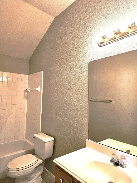 full bathroom featuring tiled shower / bath, vanity, vaulted ceiling, and toilet