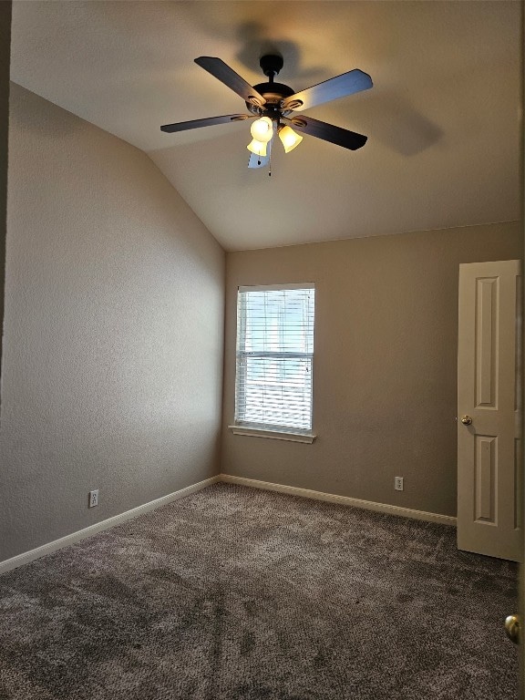 spare room featuring dark colored carpet, ceiling fan, and vaulted ceiling